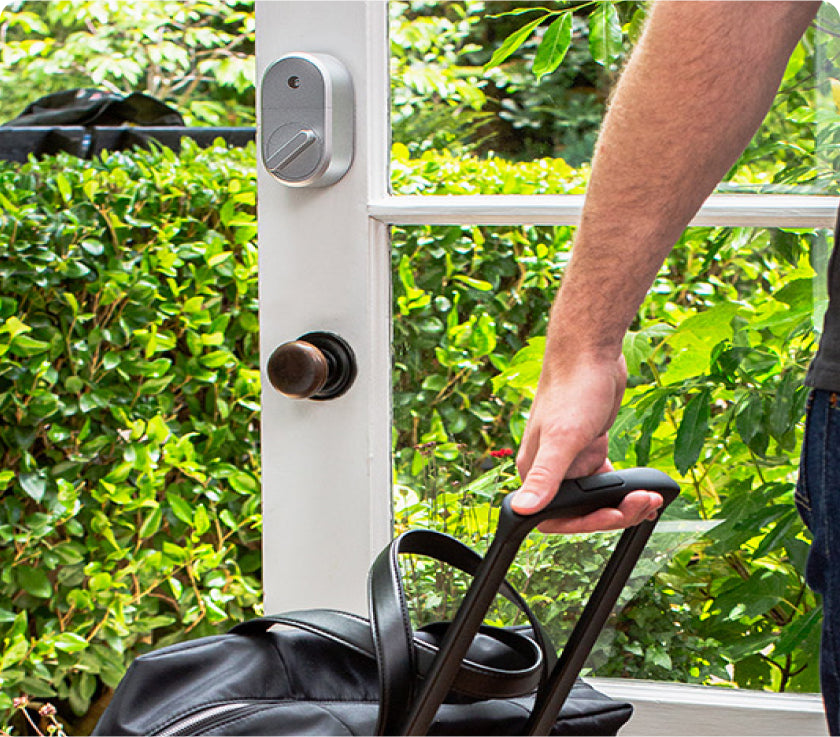 Man bringing luggage through a door with an August smart deadbolt lock installed