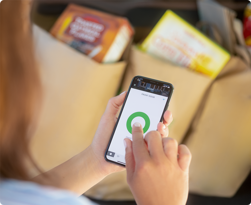 Woman unlocking her door with the August smartphone app while taking groceries out of her car.