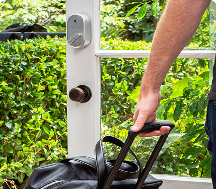 Man bringing luggage through a door with an August smart deadbolt lock installed 