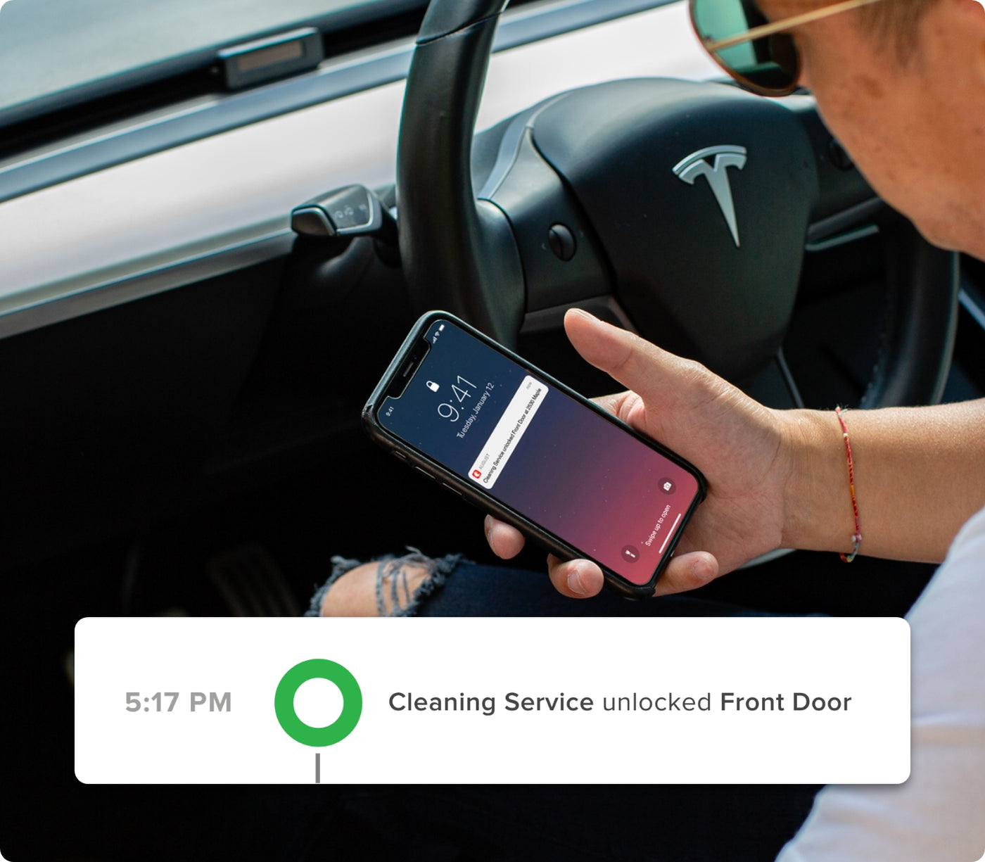A man in a tesla receiving a notification on his smartphone that the cleaning service has unlocked his front door